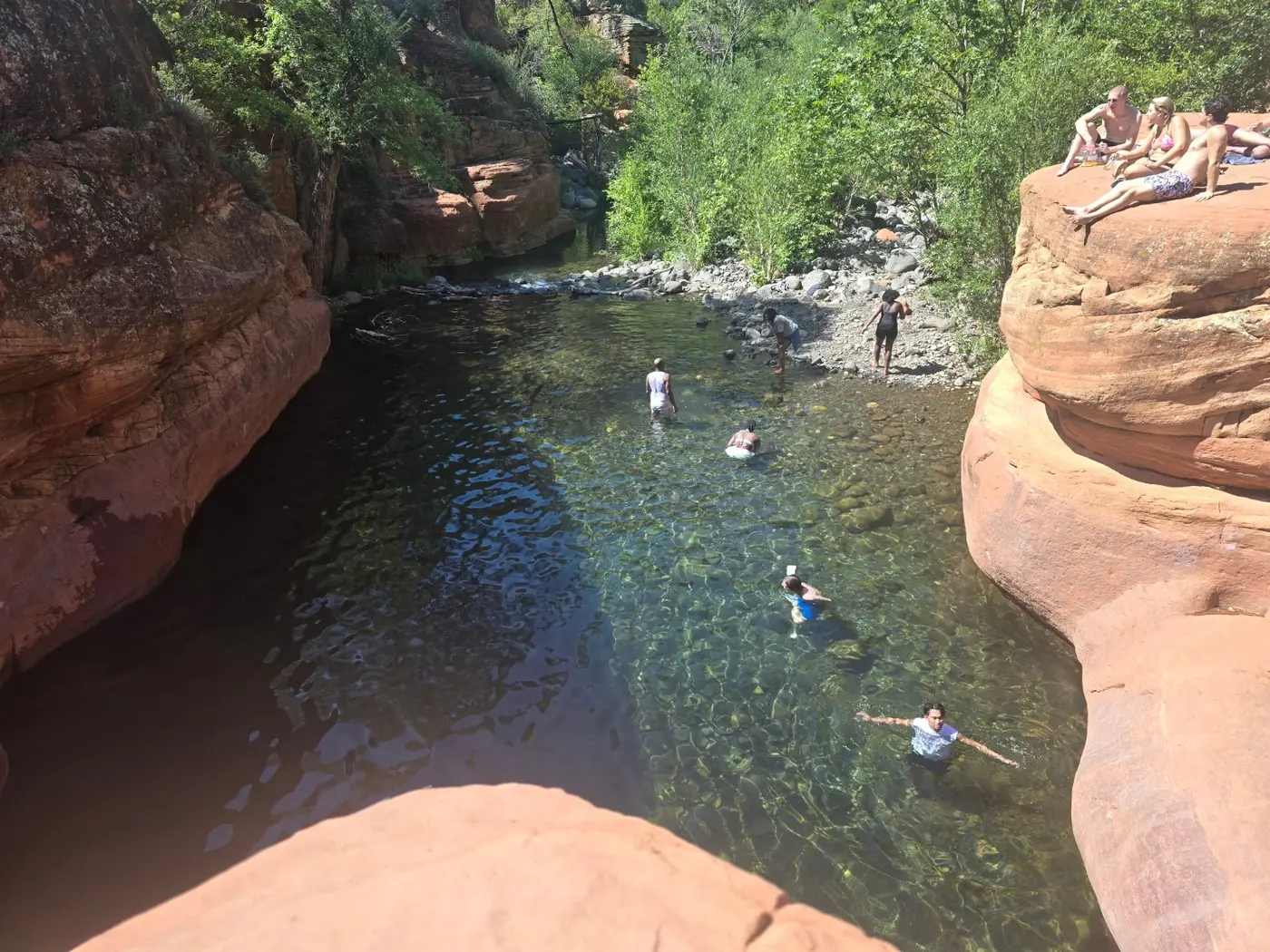 Swimmers in the clear pool between red sandstone walls at The Crack